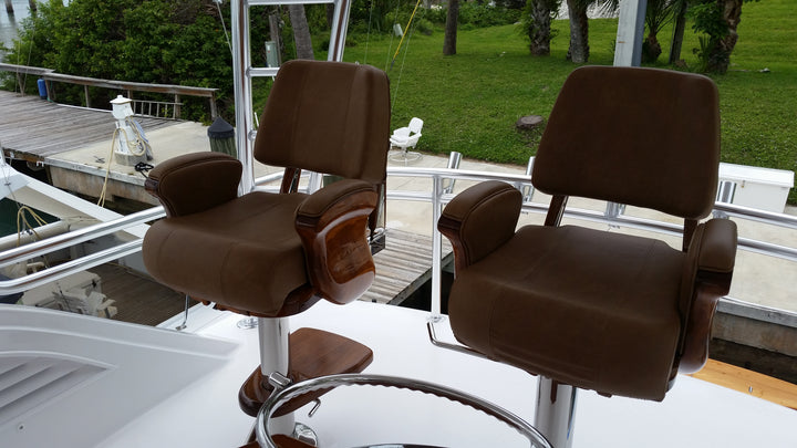 Pair of brown upholstered helm chairs with wood armrests and chrome pedestals on a boat deck