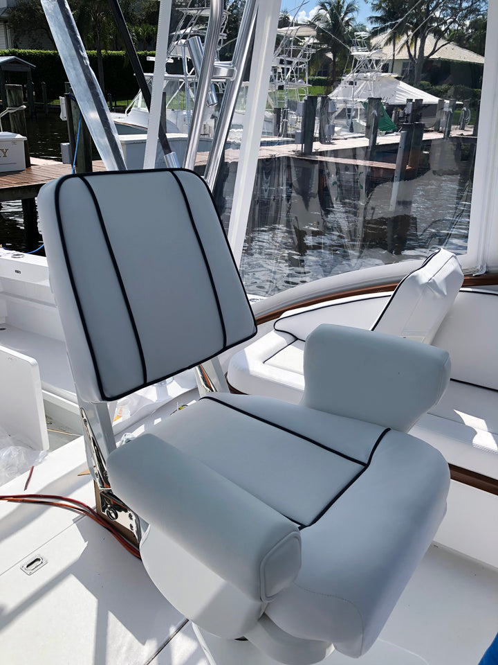 Light gray helm chair with dark contrasting piping and vertical backrest panels beside a marina
