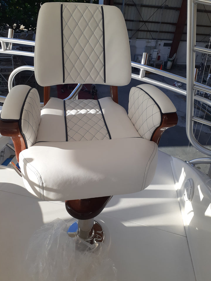 White diamond-quilted helm chair with dark piping, wood armrests, and a footrest on a boat deck