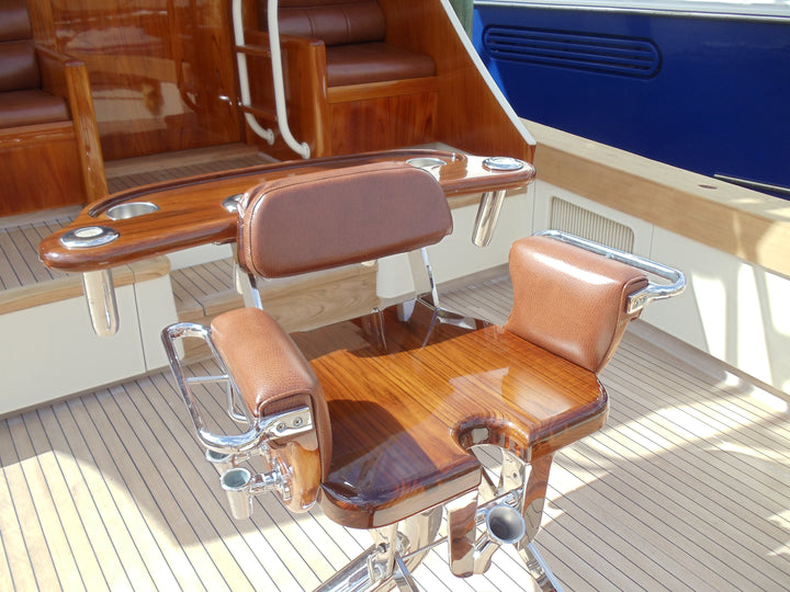 Varnished wood captain’s chair with reddish-brown upholstered backrest and arm pads above a teak deck