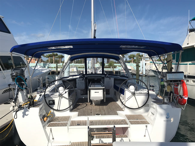 Sailboat cockpit with twin helms, a navy Bimini top, and a clear forward dodger