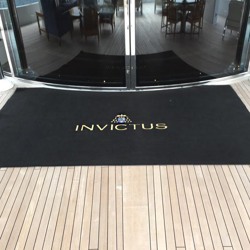 Wide black Invictus yacht entrance mat with gold name and crest outside curved salon doors