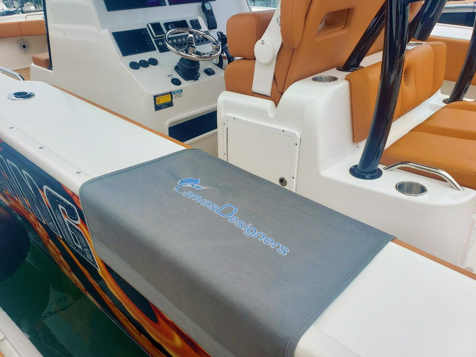 Gray embroidered boarding mat positioned on a boat gunwale beside tan helm seating
